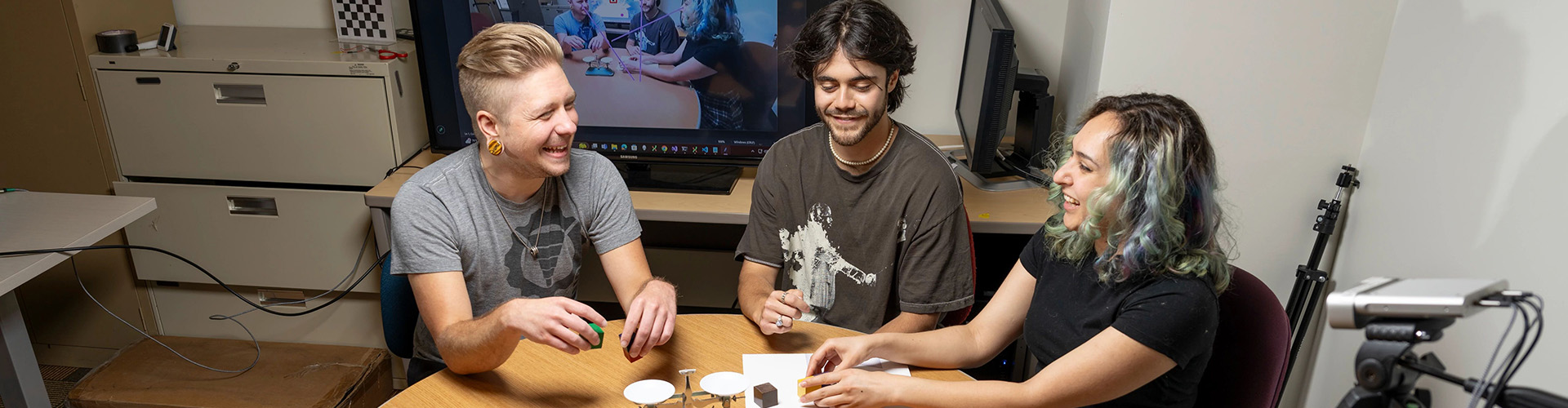 Student researchers training an AI agent Student researchers sitting at a table moving blocks and objects to train an AI agent.